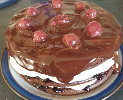 A black forest gateau topped with glace cherries under a chocolate glaze