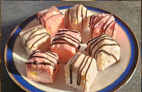 Iced fondant fancies drizzled with chocolate on a blue-rimmed plate