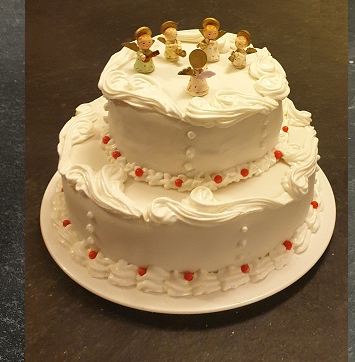 A two-tier white cake piped with scrollwork and topped with gold angel figures
