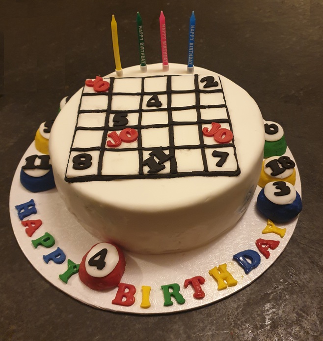 A white cake topped with a sugar bingo card and ringed with numbered bingo balls