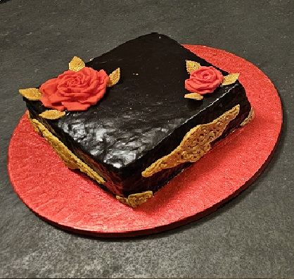 A dark chocolate-glazed cake decorated with red sugar roses and gold leaves