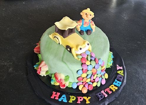A green birthday cake with a sugar digger, a teddy and chocolate beans