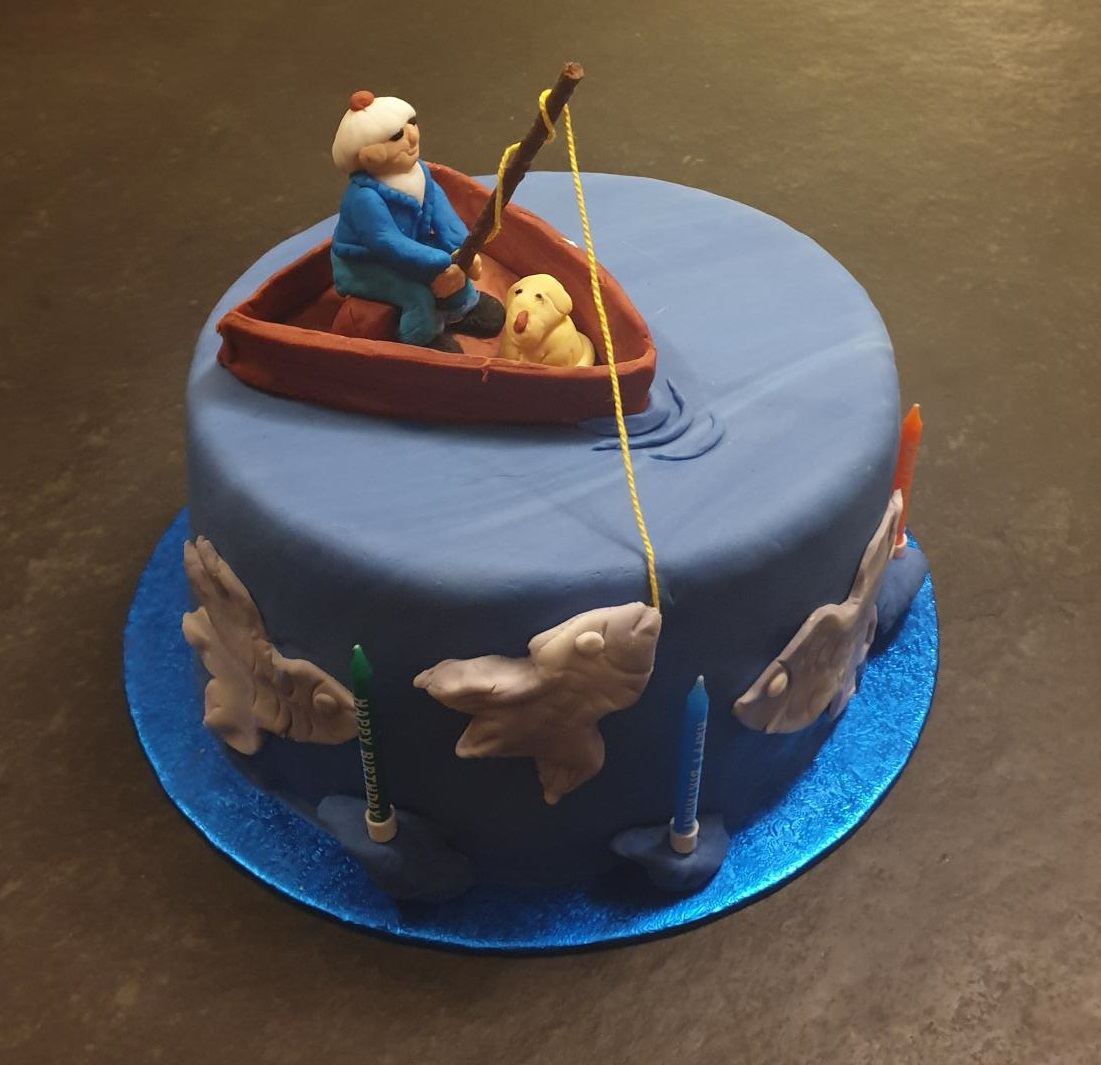A blue birthday cake modelled with a sugar fisherman in a rowing boat