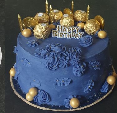 A navy blue birthday cake topped with gold-wrapped chocolates and candles