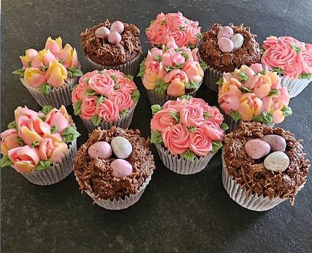 Cup cakes piped with buttercream flowers alongside chocolate nest cakes