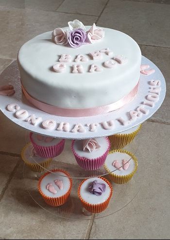 A christening cake on a stand with matching cup cakes below