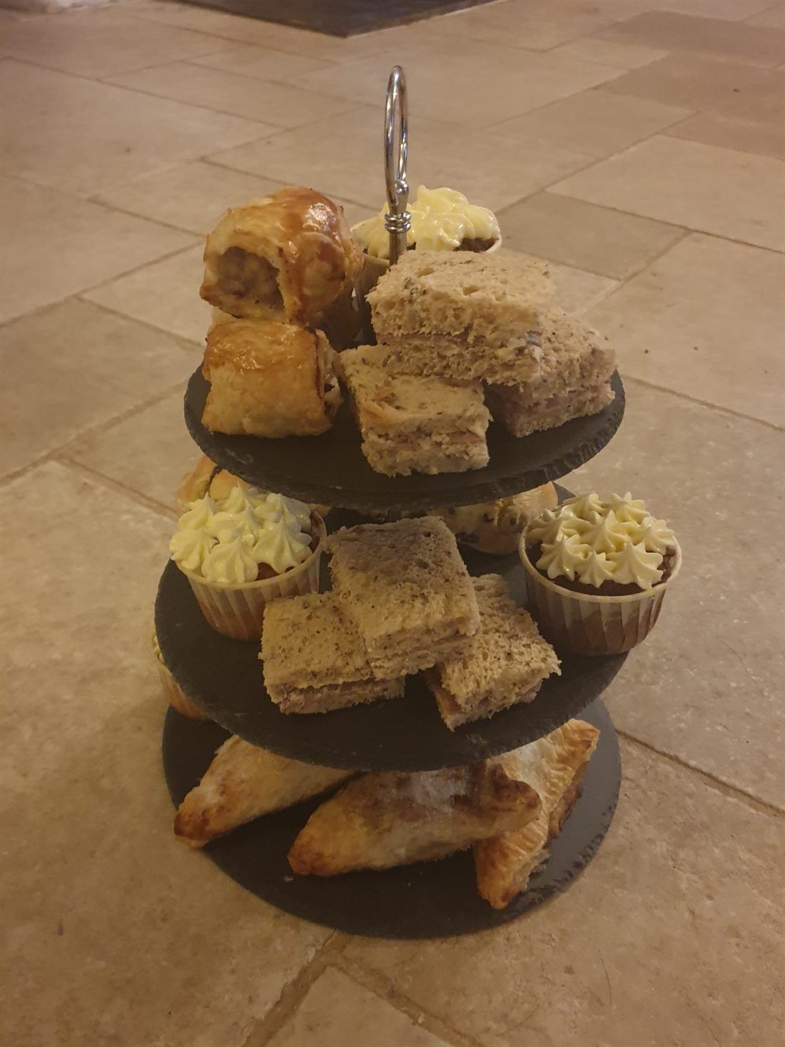 A three-tier high tea stand of sausage rolls, sandwiches and cup cakes